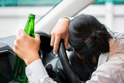 Person passed out in a car with a green bottle, symbolizing impaired driving or DWI.