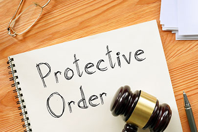 A notepad with Protective Order written on it next to a gavel and glasses, representing a legal protective order.