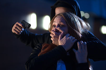 A masked person holds a gun to a terrified woman's head, illustrating an aggravated assault.